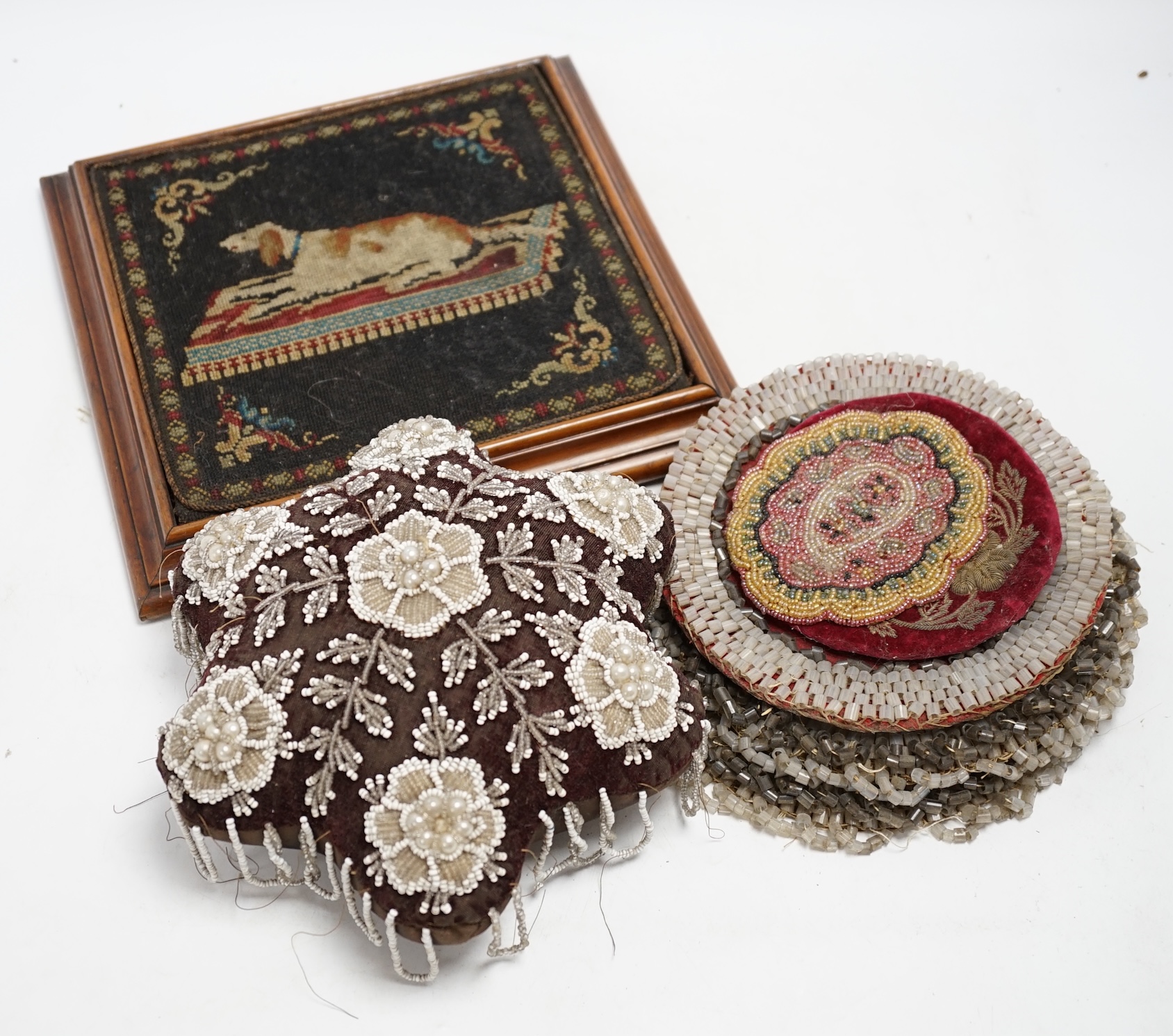 A 19th century framed needlework panel of a dog (possibly a teapot stand), a collection of bead worked mats, a beaded and tasselled tie-back and a large pin cushion, dog needlework 22.5cm wide. Condition - some beads mis